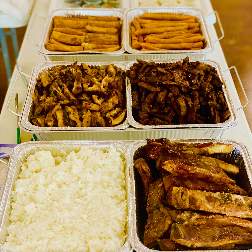 Toa's Ohana Hawaiian catering spread with ribs, chicken, rice, and sweet potato fries in foil trays.