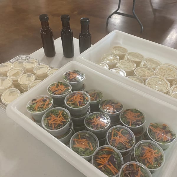 Pre-packaged salads with shredded carrots and dressing cups, alongside three dark bottles of sauce.