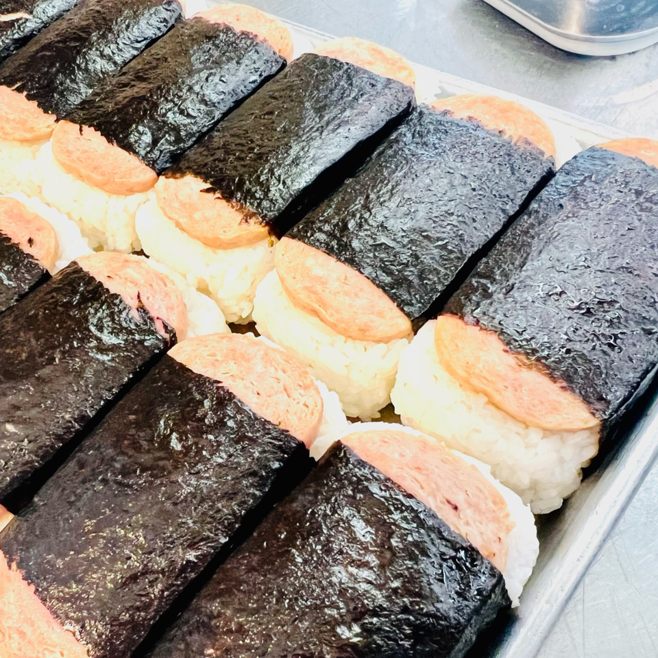 A tray filled with rows of Toa's Ohana Hawaiian Restaurant's Spam Musubi, featuring grilled Spam on rice wrapped in nori.