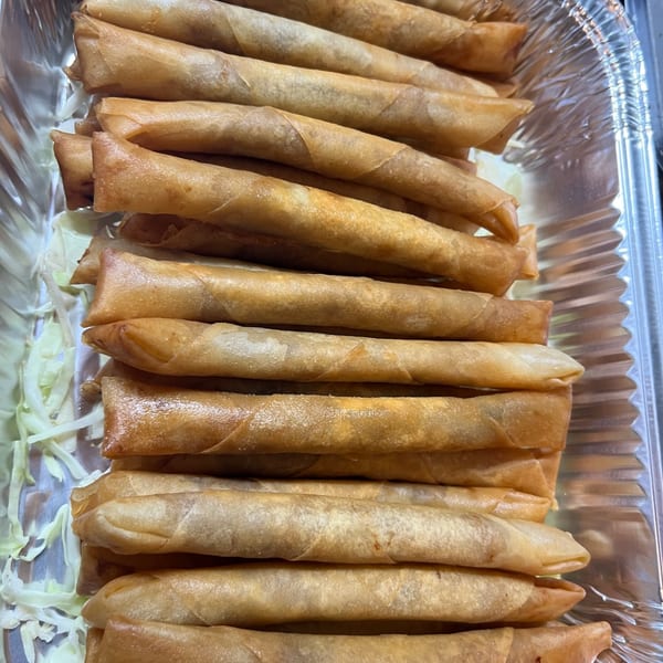 Crispy golden-brown lumpia spring rolls, stacked in a foil tray with shredded cabbage.