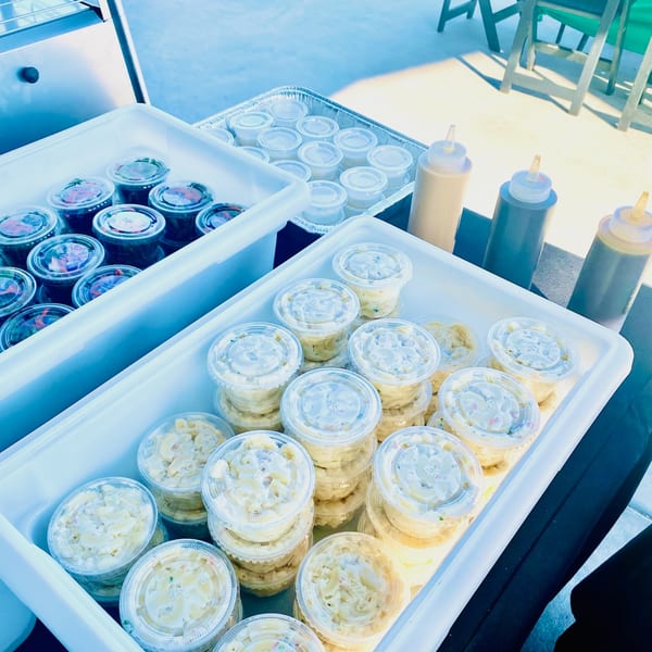 To-go containers of Hawaiian macaroni salad and other dishes, with squeeze bottles of sauces.