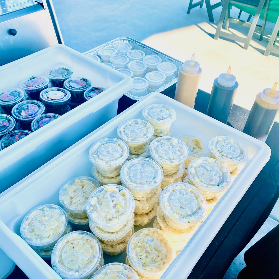 To-go containers of Hawaiian macaroni salad and other dishes, with squeeze bottles of sauces.